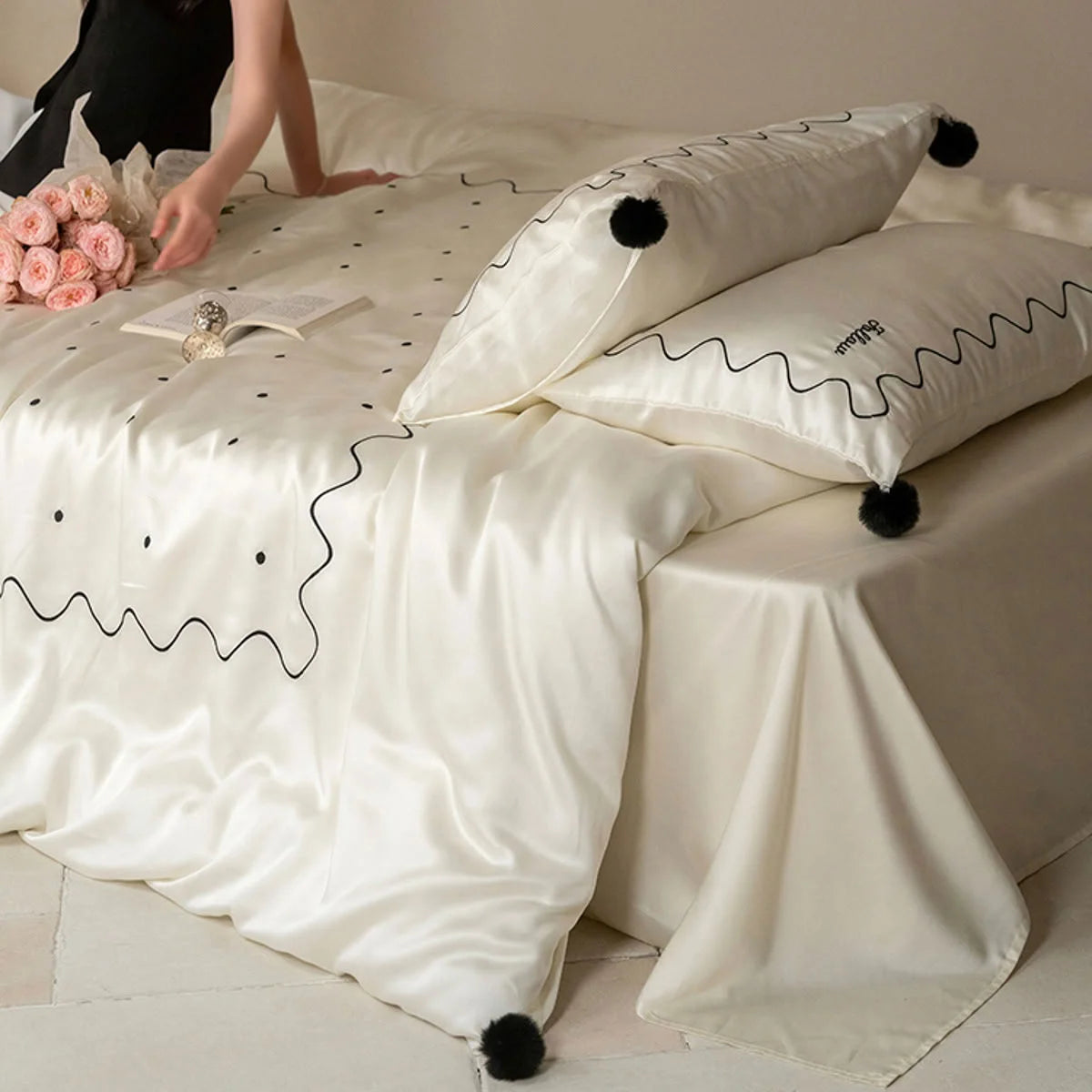 A woman arranging pink roses on a bed with the Creamy White & Black silky Tencel bedding set. - RoomDen