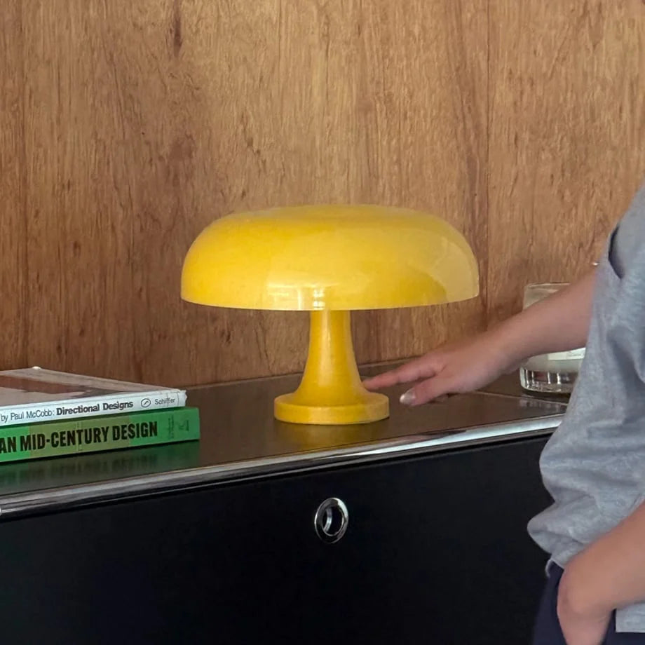Close-up of a hand reaching for the marigold yellow mushroom lamp on a black cabinet - RoomDen.