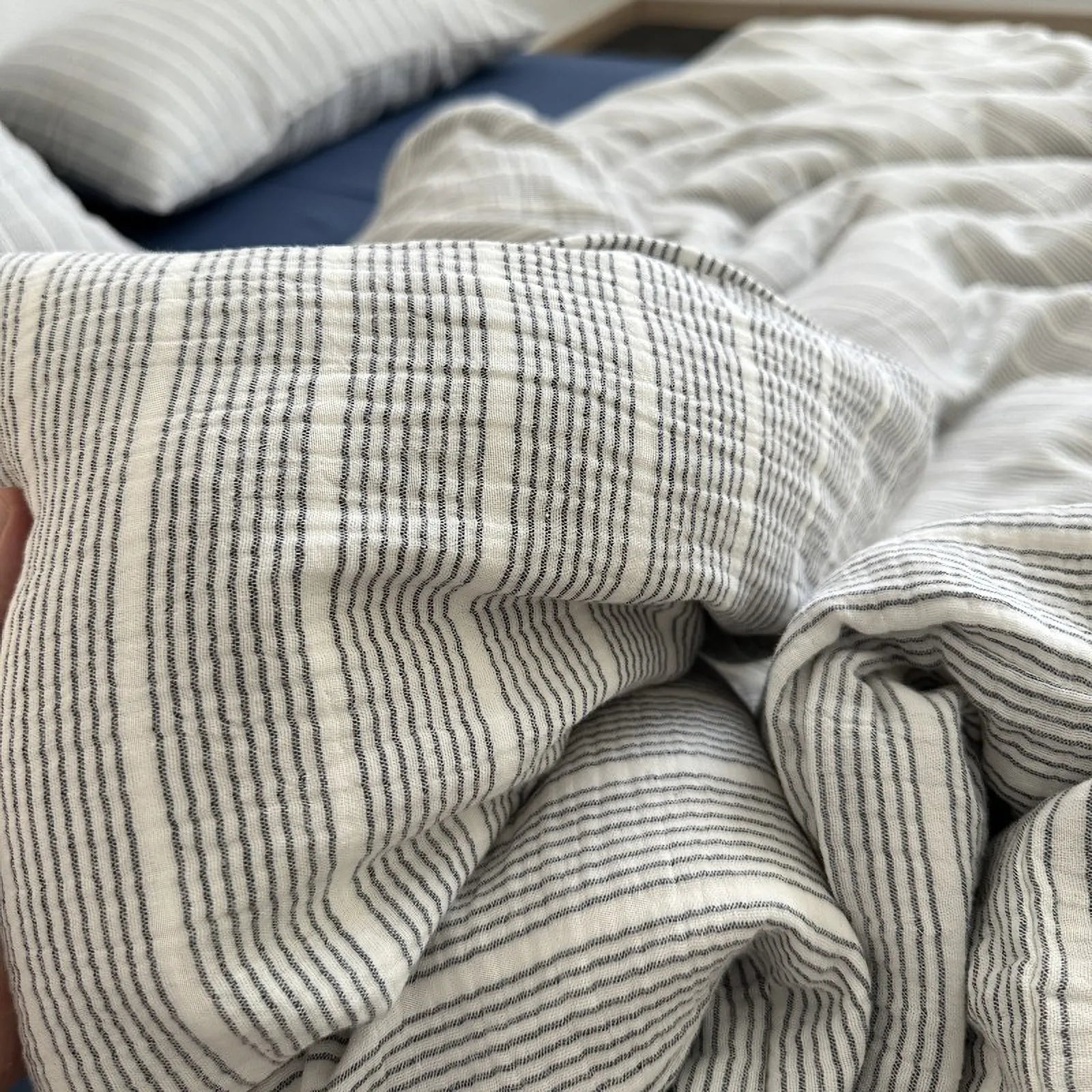 Hand holding the soft, crinkled fabric of the grey pinstripe washed cotton duvet cover.