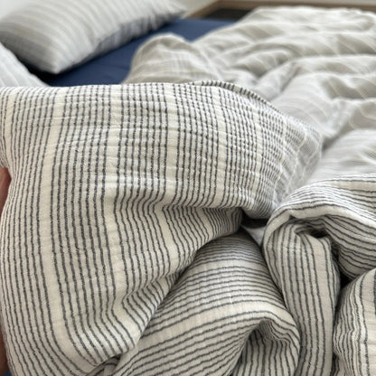 Hand holding the soft, crinkled fabric of the grey pinstripe washed cotton duvet cover.