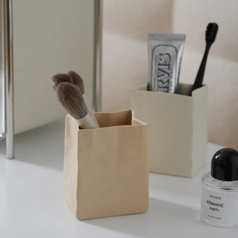 A khaki and a cream crumpled ceramic organizer on a bathroom counter holding makeup brushes and a toothbrush. - RoomDen