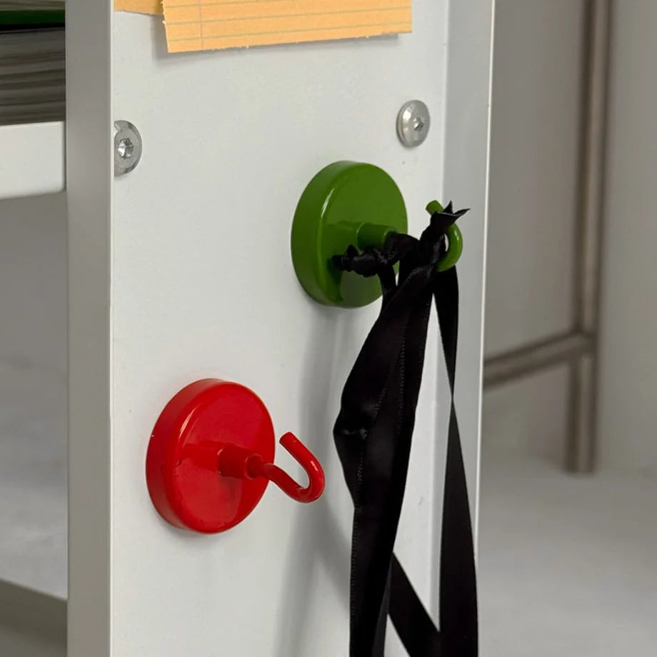 Red and green magnetic metal hooks on a white shelf, with the green hook holding a black ribbon - RoomDen