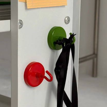 Red and green magnetic metal hooks on a white shelf, with the green hook holding a black ribbon - RoomDen
