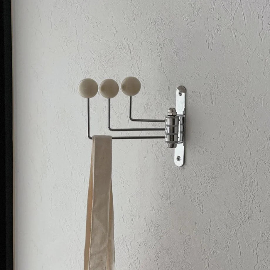 Side profile of the cream swivel wall hook with its arms folded, next to a dark door frame - RoomDen.