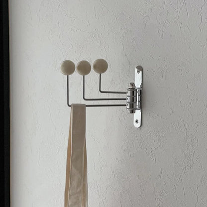 Side profile of the cream swivel wall hook with its arms folded, next to a dark door frame - RoomDen.