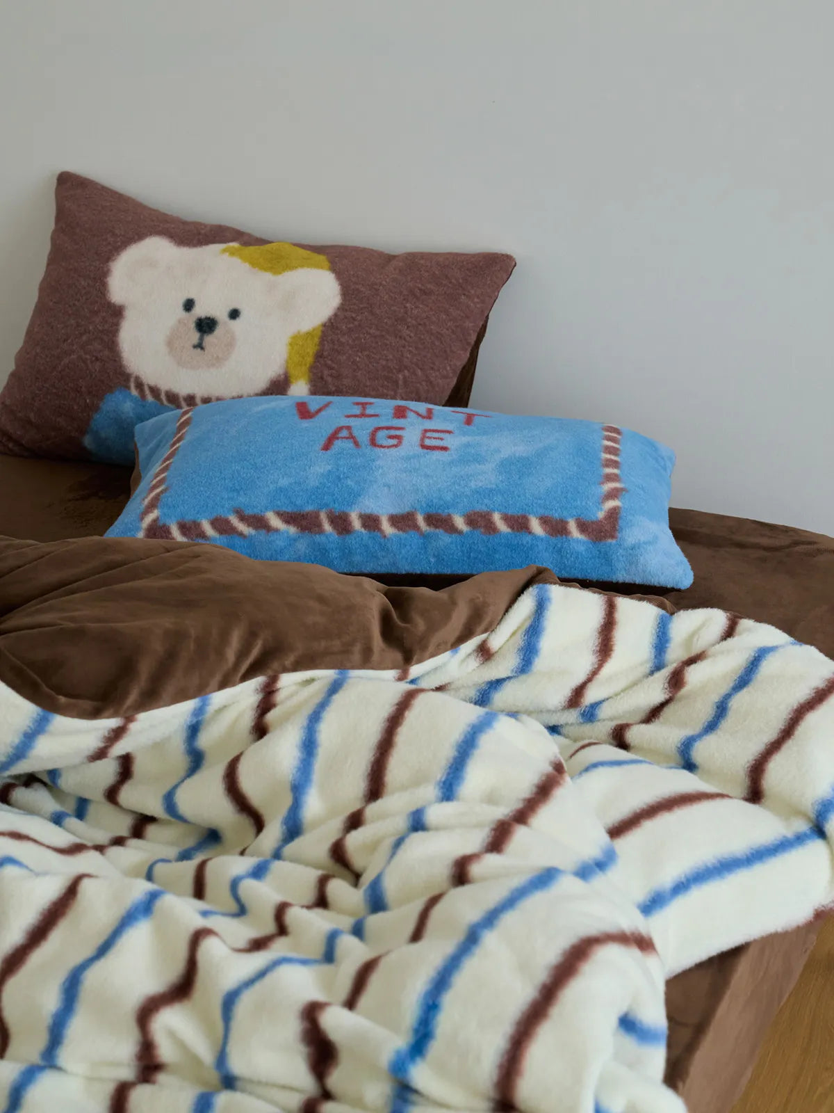 Cozy bedroom scene featuring the Vintage Bear Striped Flannel Fleece Bedding Set, with pillows stacked against a white wall. - RoomDen
