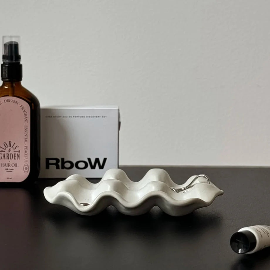 White Speckled Wavy Ceramic Jewelry Dish on a desk next to a hair oil bottle and perfume box.
