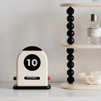 The perpetual desk calendar displayed on a white surface next to a modern black beaded shelf - RoomDen