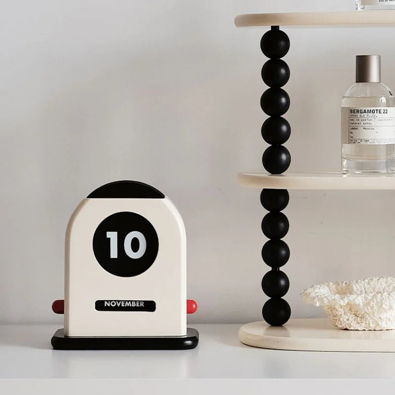 The perpetual desk calendar displayed on a white surface next to a modern black beaded shelf - RoomDen