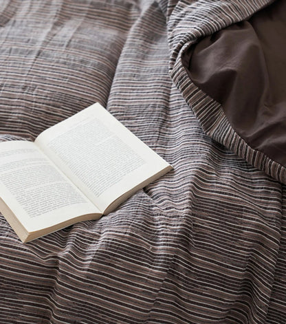 Close-up on the texture of the Mocha Brown pinstripe bedding with an open book resting on it - RoomDen