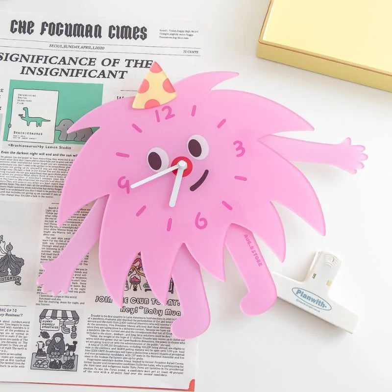 The whimsical pink monster clock displayed on a newspaper, showing its fun character design.