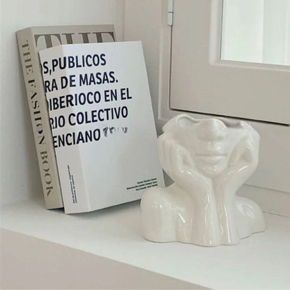 White abstract face vase styled next to fashion books on a white shelf - RoomDen.