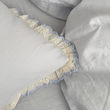 Macro shot of the corner of a pillowcase, highlighting the intricate eyelet embroidery and ruffle detail of the bedding set.