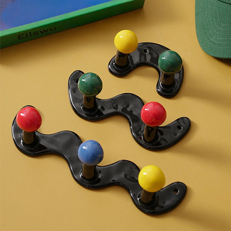 Assortment of black wavy ceramic hooks with multicolor balls on a mustard yellow surface.