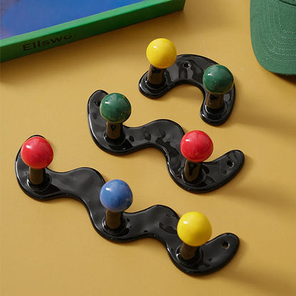 Assortment of black wavy ceramic hooks with multicolor balls on a mustard yellow surface.