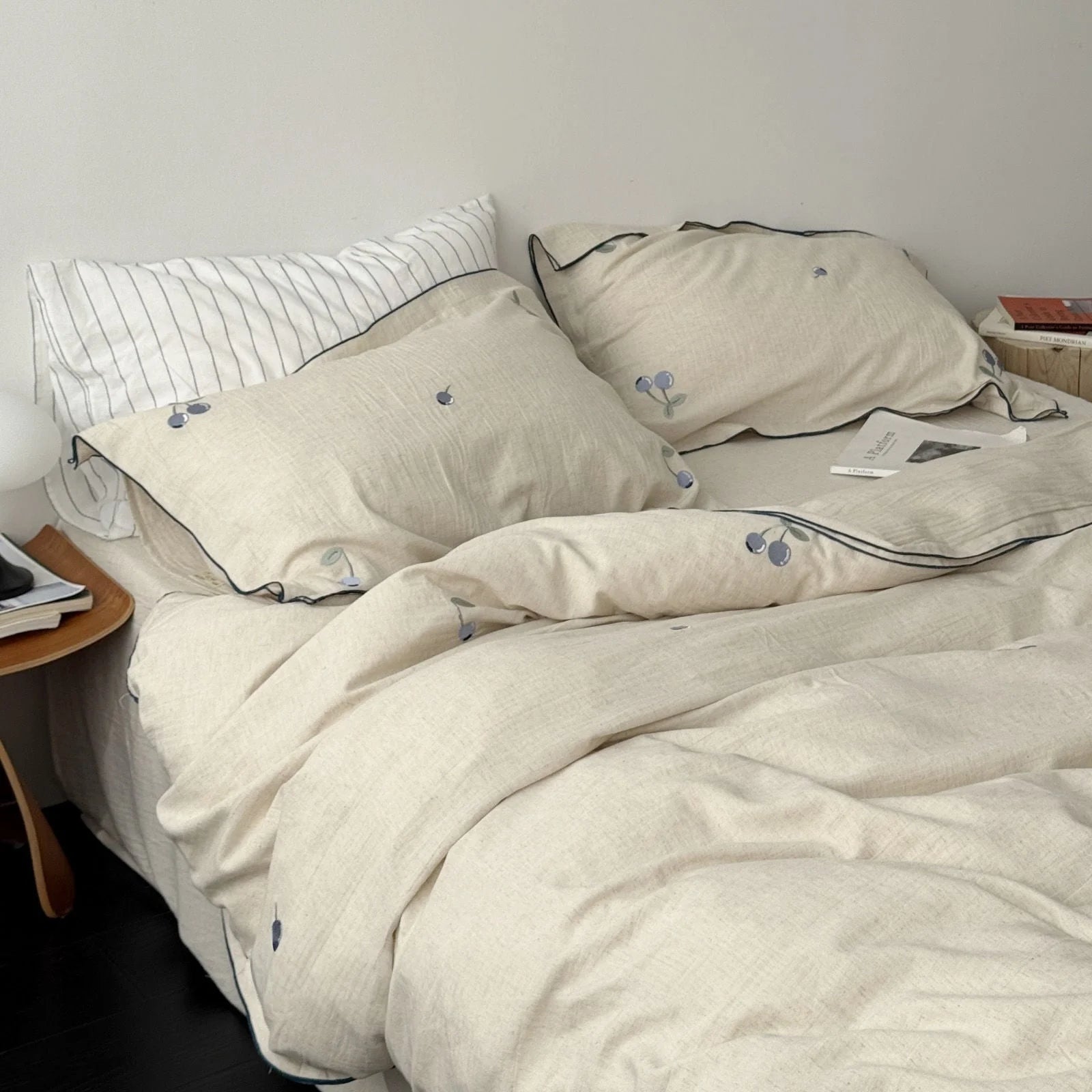 Angled shot of the blueberry embroidered linen bedding set, showing how it drapes on the bed in a minimalist bedroom. - RoomDen