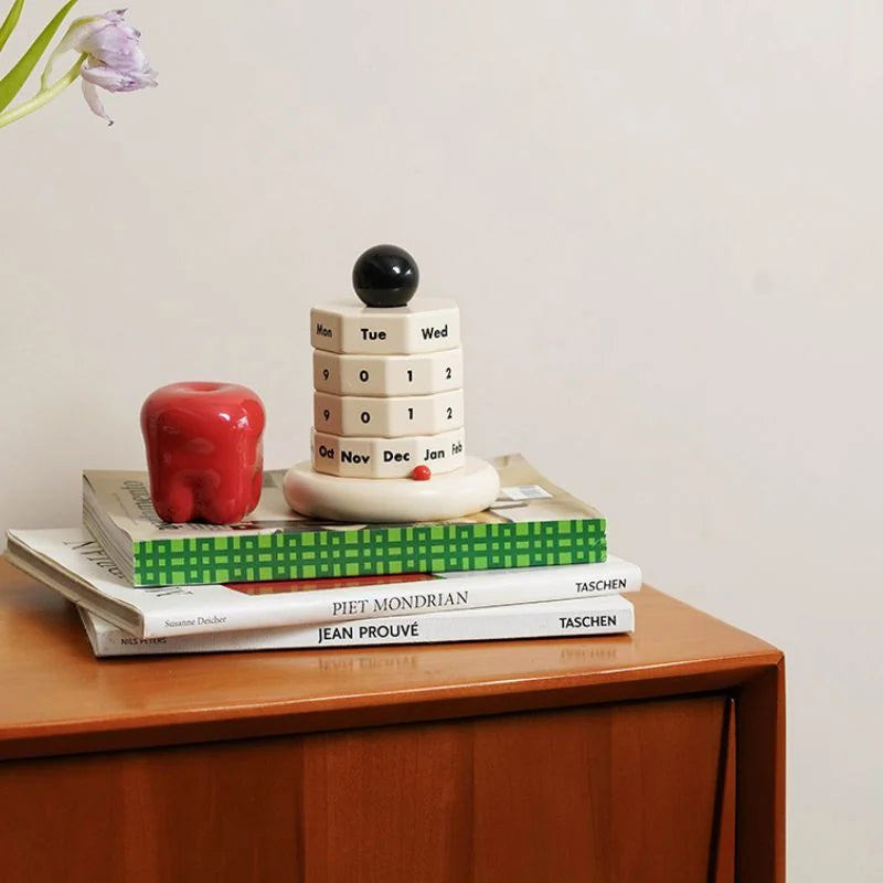 The perpetual calendar styled on a wooden dresser with books and a red apple decor piece. - RoomDen