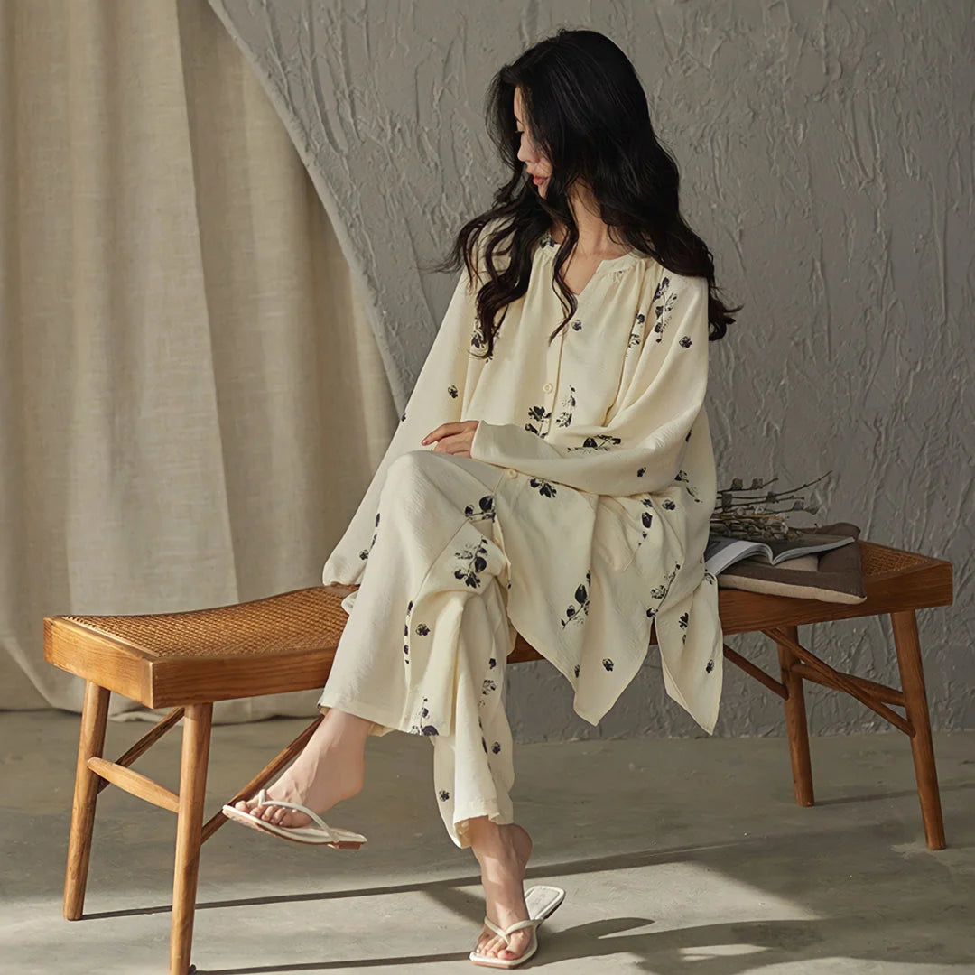 Full view of the relaxed-fit botanical print pajama set, model sitting on a woven wooden bench - RoomDen