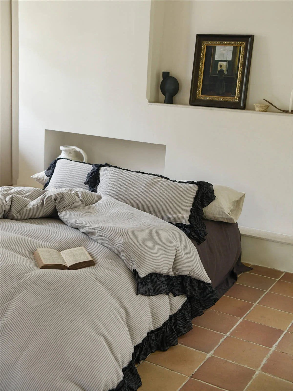 Lifestyle shot of the pinstripe ruffle bedding set with a book, highlighting the cozy bedroom aesthetic. - RoomDen