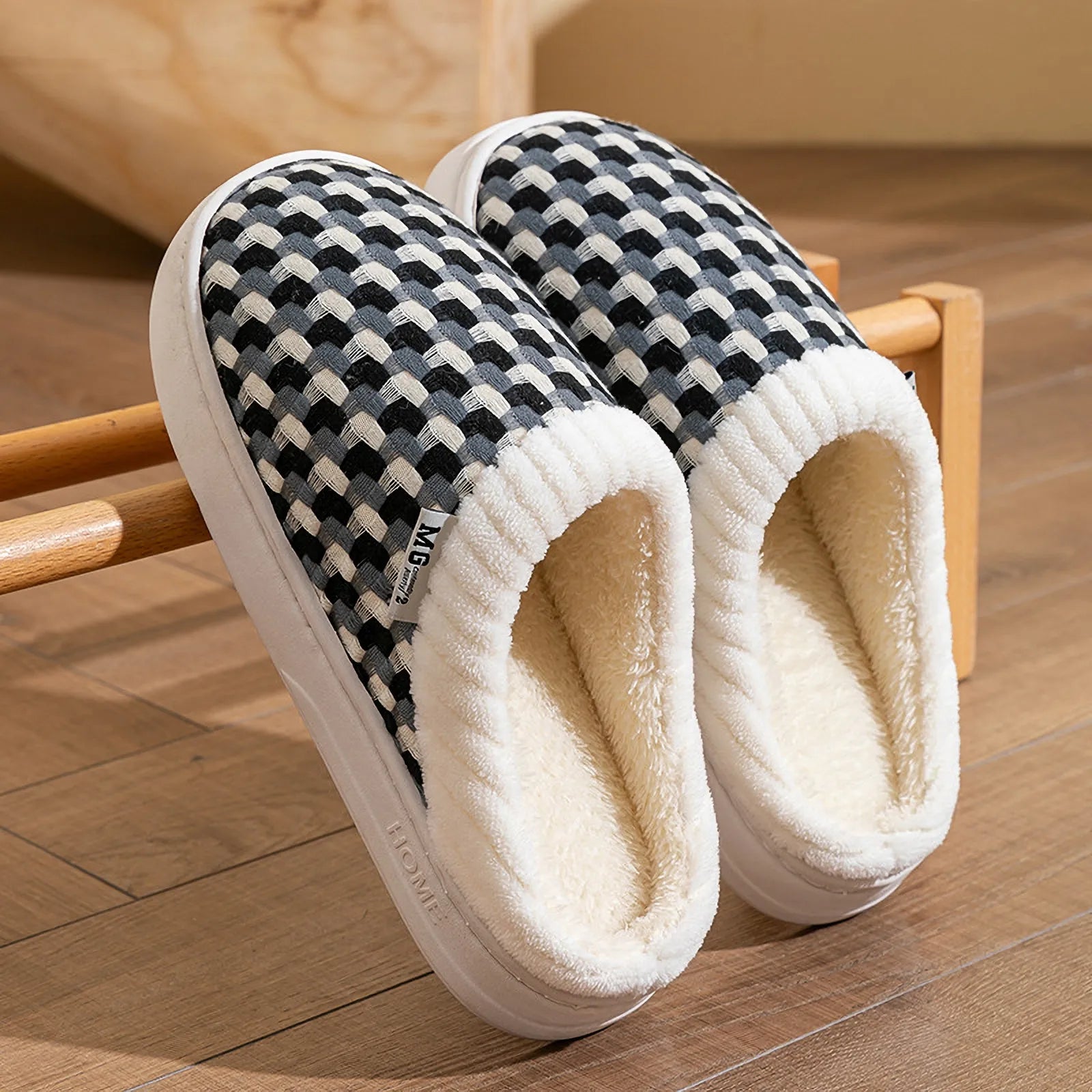 Pair of black and white woven plush slippers resting on wooden rack