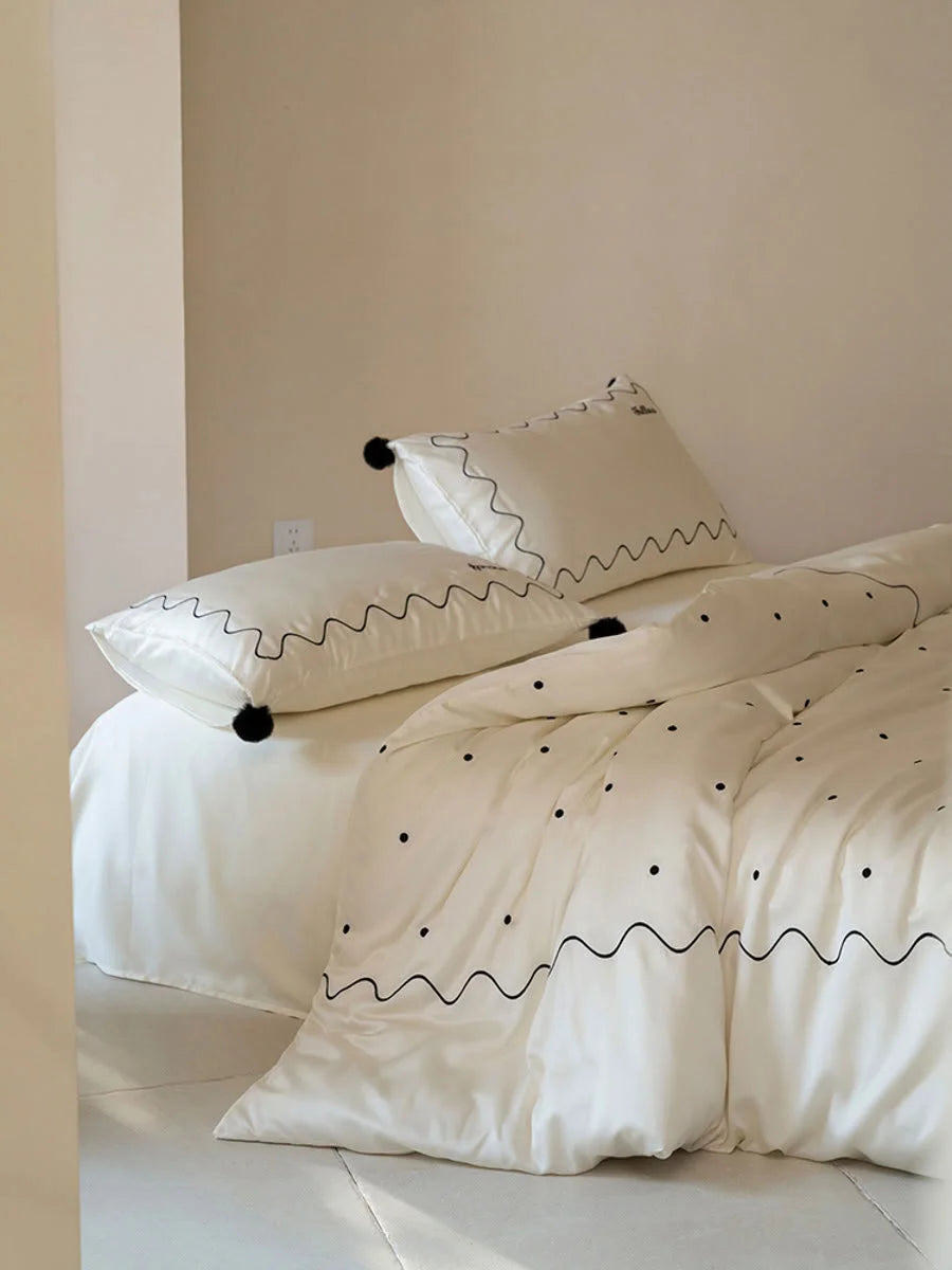 Angled view of the Creamy White & Black embroidered Tencel bedding set, highlighting the black pom poms. - RoomDen
