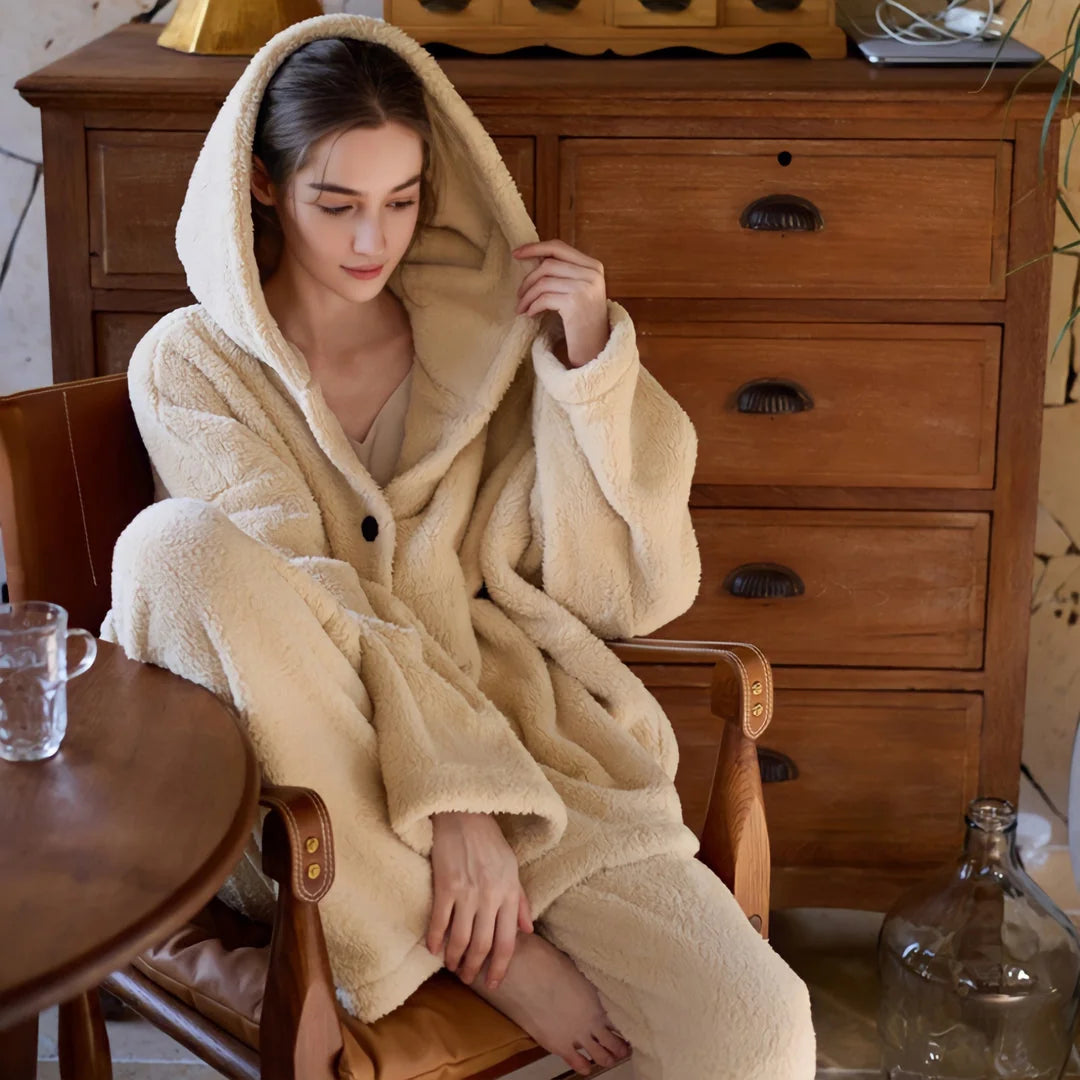 Model curled up in a chair, touching the hood of her plush beige pajama set. - RoomDen