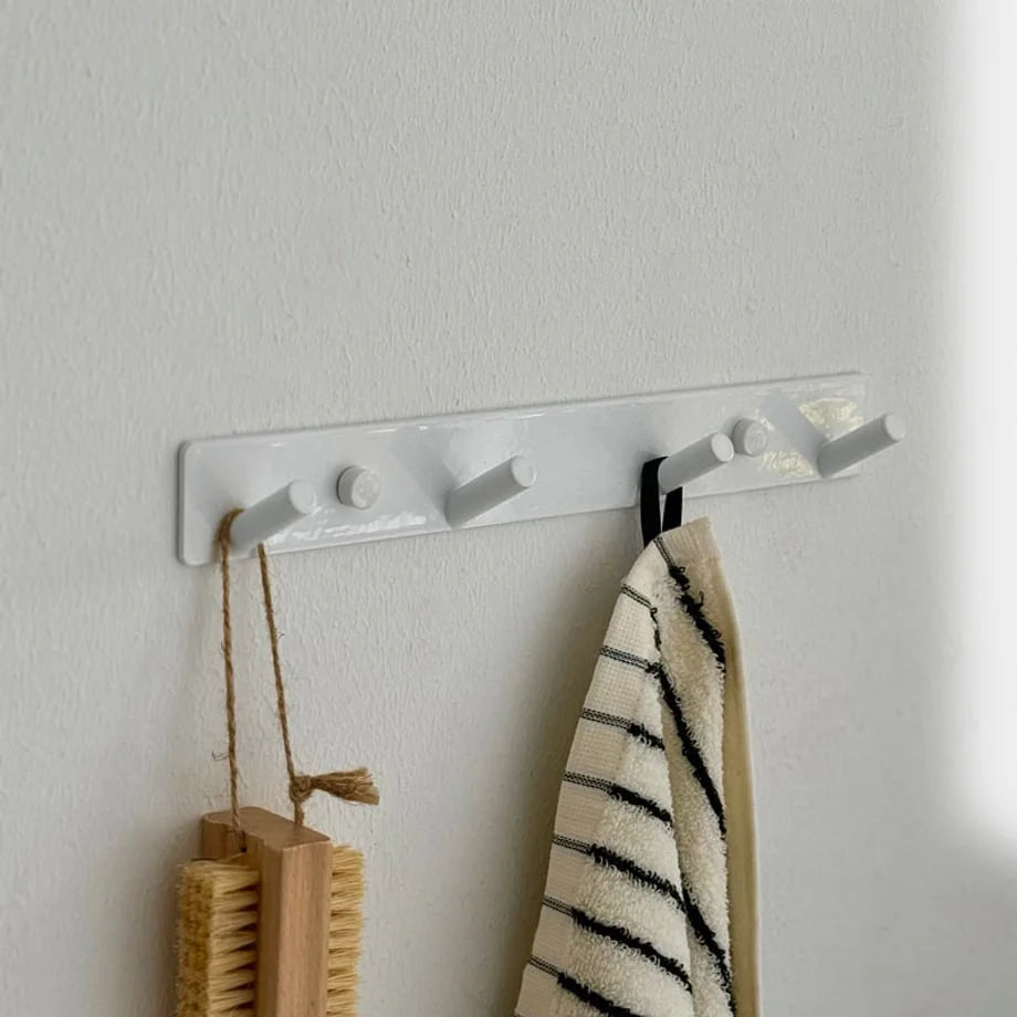 Angled shot of the white metal wall hook rack mounted on a white textured wall - RoomDen.