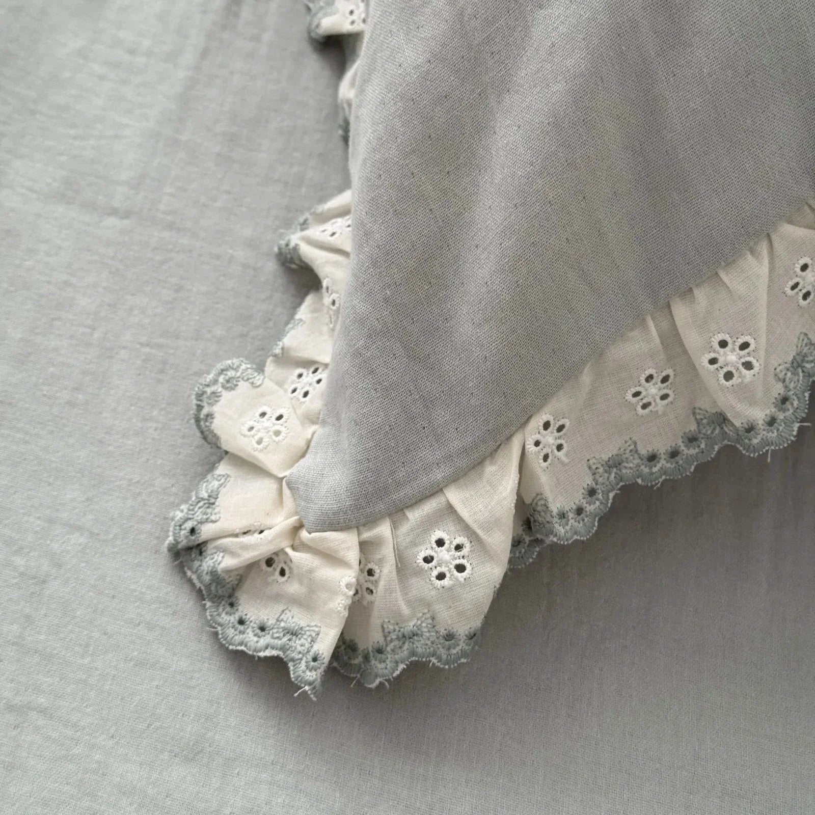 Detailed close-up of the embroidered lace ruffle trim on the sage green pillowcase, showing the fabric's texture.