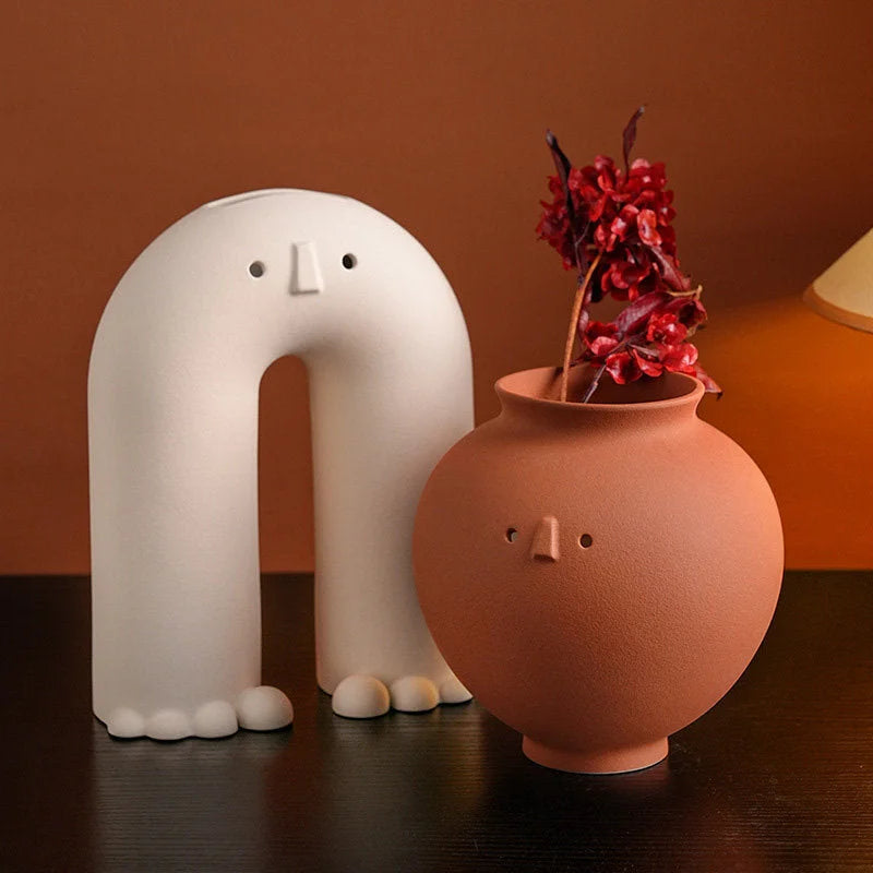 The Arch and Pot Frosted Minimalist Face Vases on a dark wood table, with a red dried flower in the Pot vase. - RoomDen