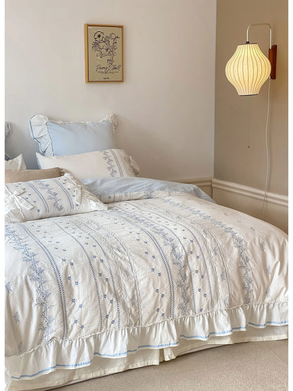 Ruffled Floral Vine Embroidered Cotton Bedding Set in Cornflower Blue, styled in a cozy bedroom with a wall lamp. - RoomDen