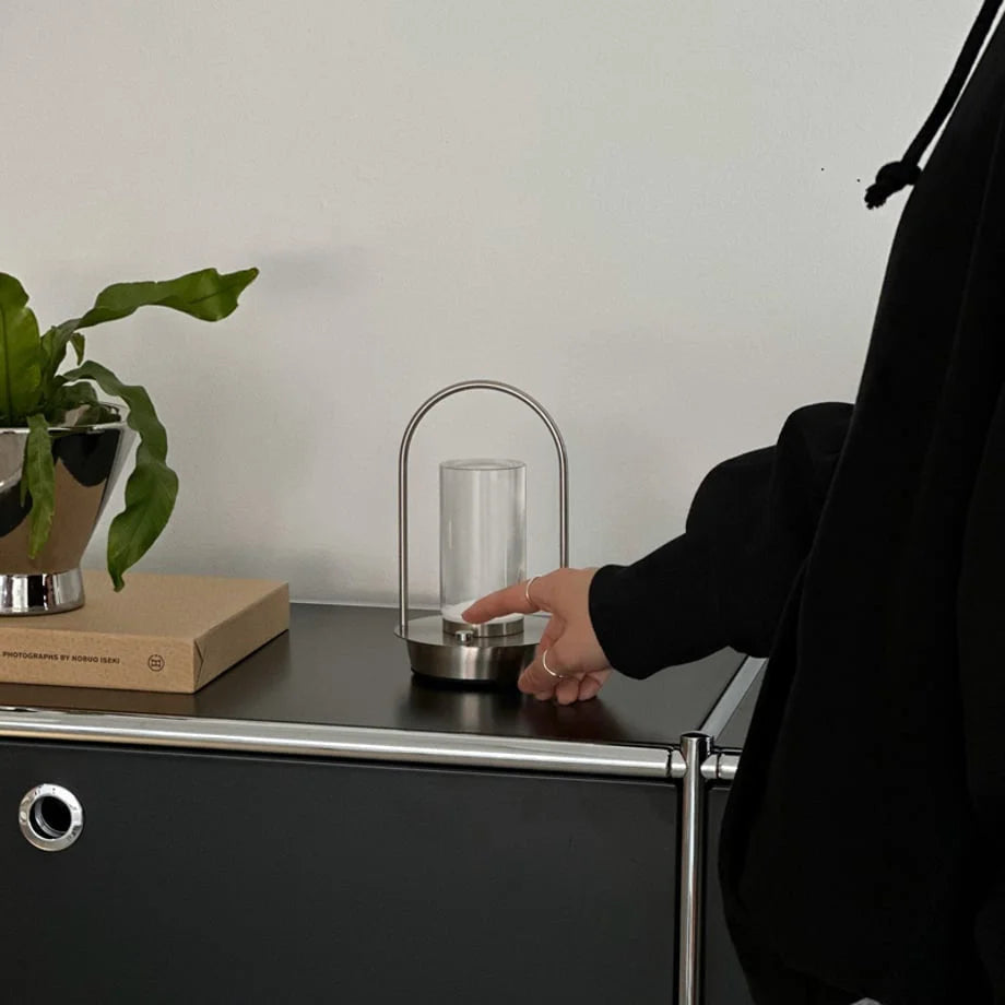 The Minimalist Arch Metal Table Lamp being turned on by touch on a black surface. - RoomDen