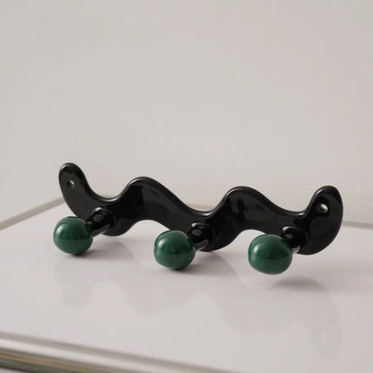 Three-hook wavy black ceramic wall rack with green balls on a white surface - RoomDen.
