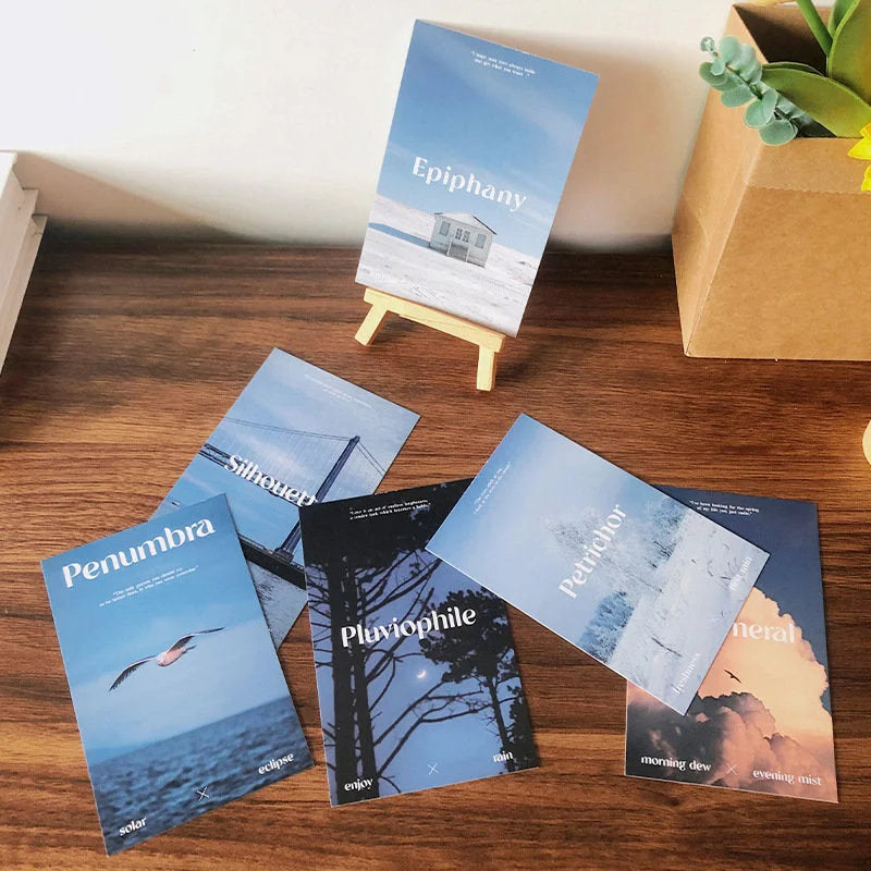 A close-up of the Poetic Photo Wall Collage Kit cards, featuring atmospheric blue sky and sea prints on a wooden desk - RoomDen