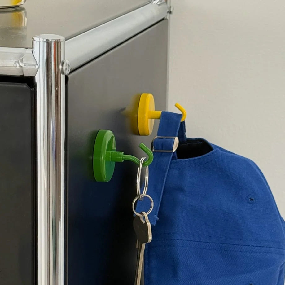 Detailed view of a yellow magnetic hook holding a blue cap and a green hook holding keys on a black cabinet - RoomDen