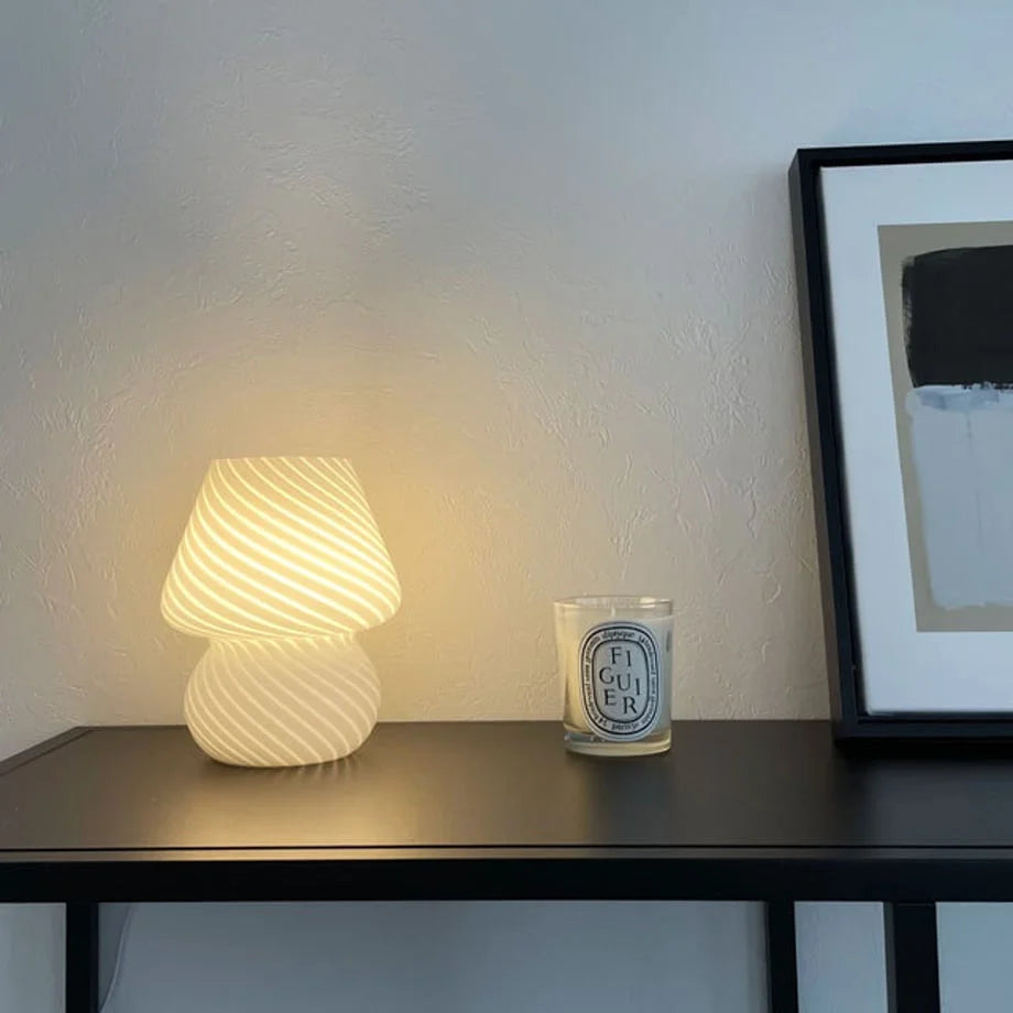 The Swirled Glass Mushroom Lamp next to a candle and framed art, creating a cozy corner - RoomDen.