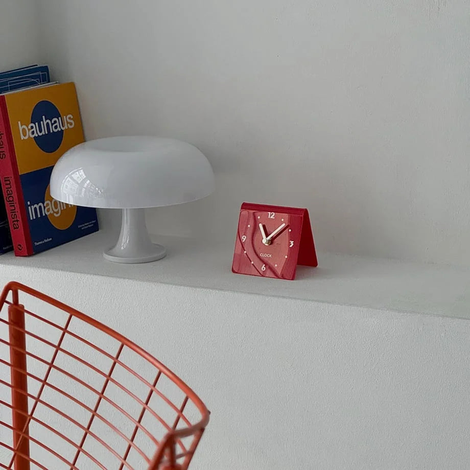Red Sleek Minimalist Metal Table Clock styled on a shelf with a white mushroom lamp and Bauhaus book. - RoomDen