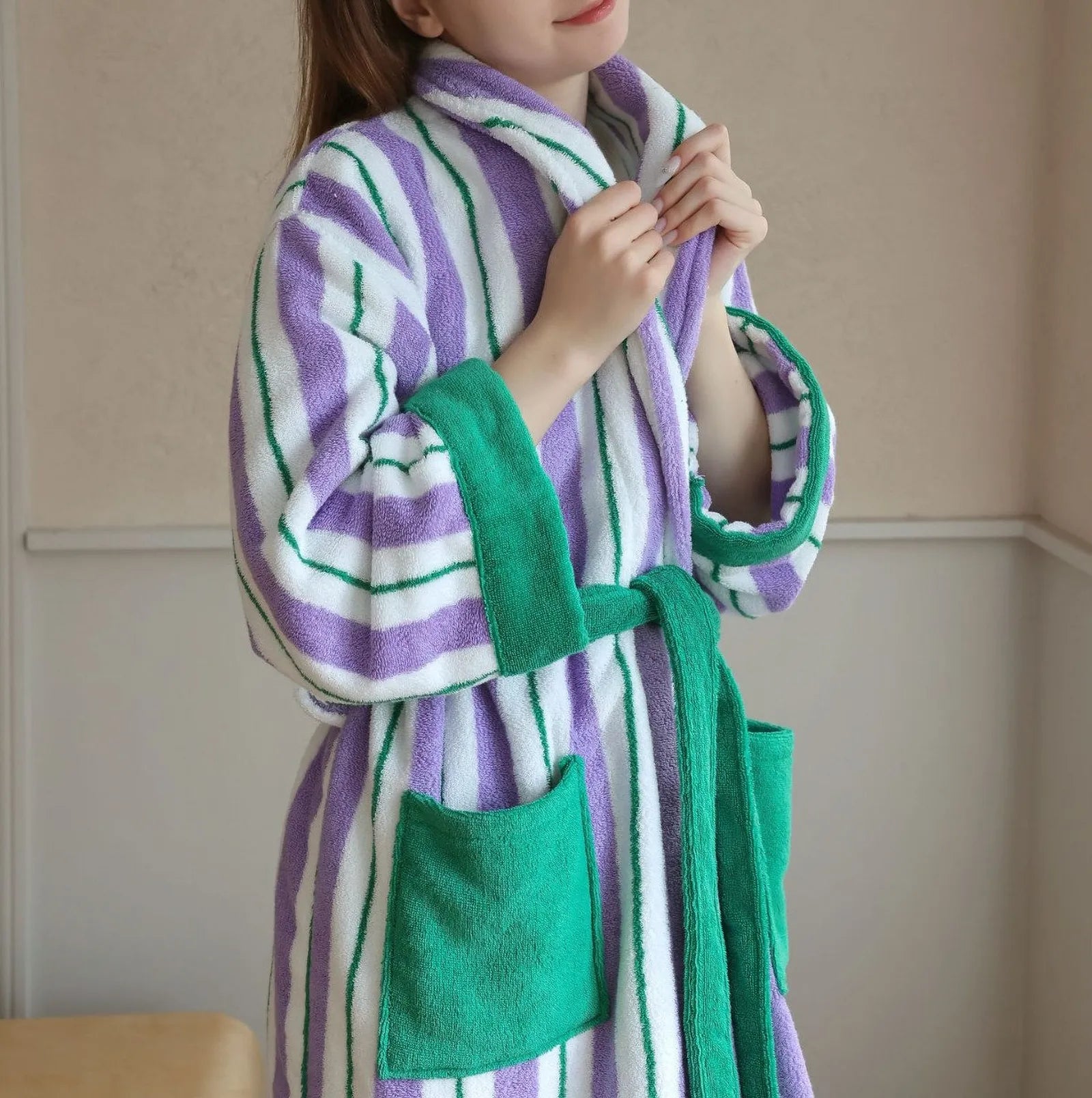 Woman wearing plush purple and white striped cotton robe with green accents tying the belt