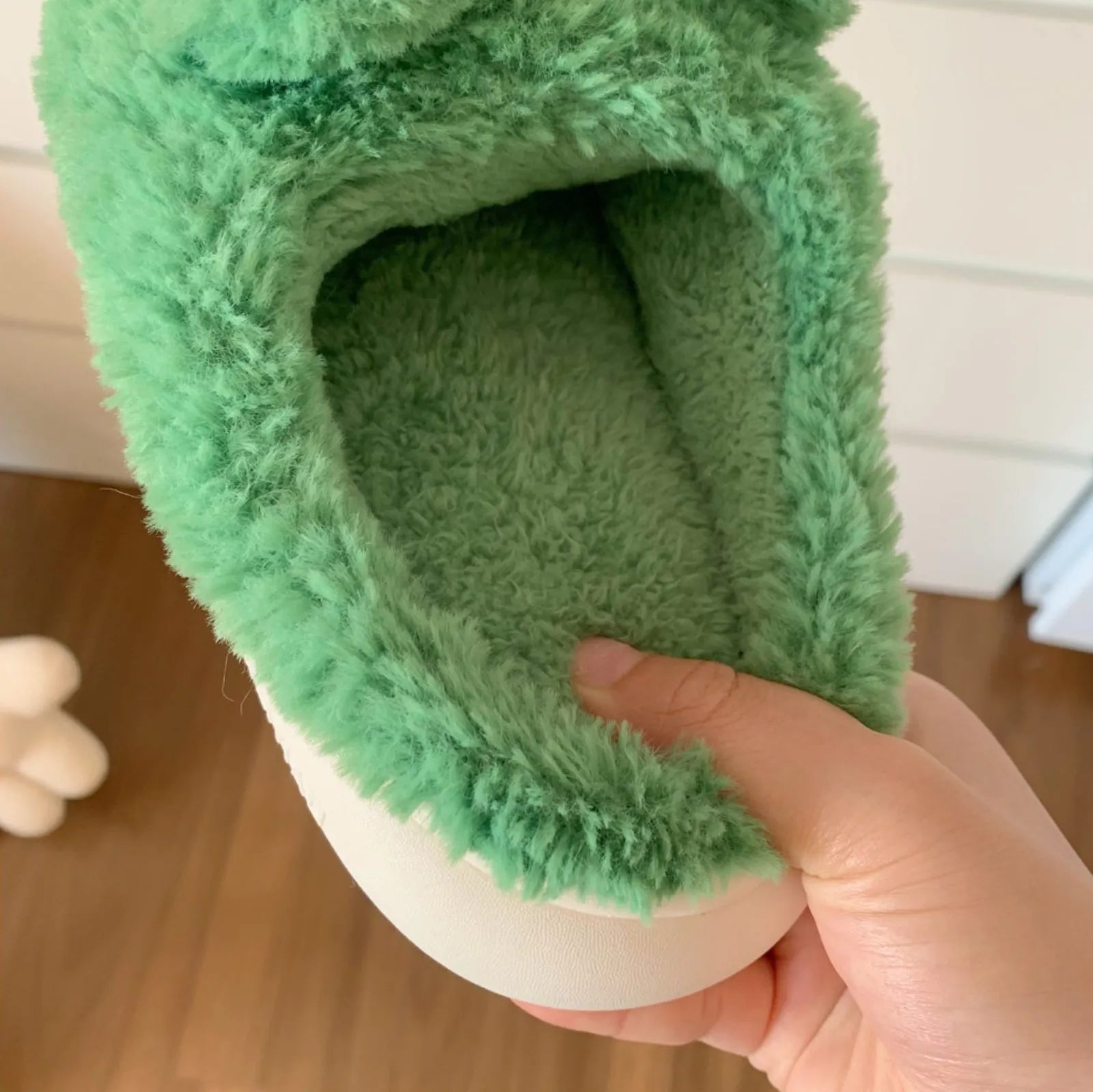 Hand holding slipper revealing soft fuzzy green interior lining - RoomDen