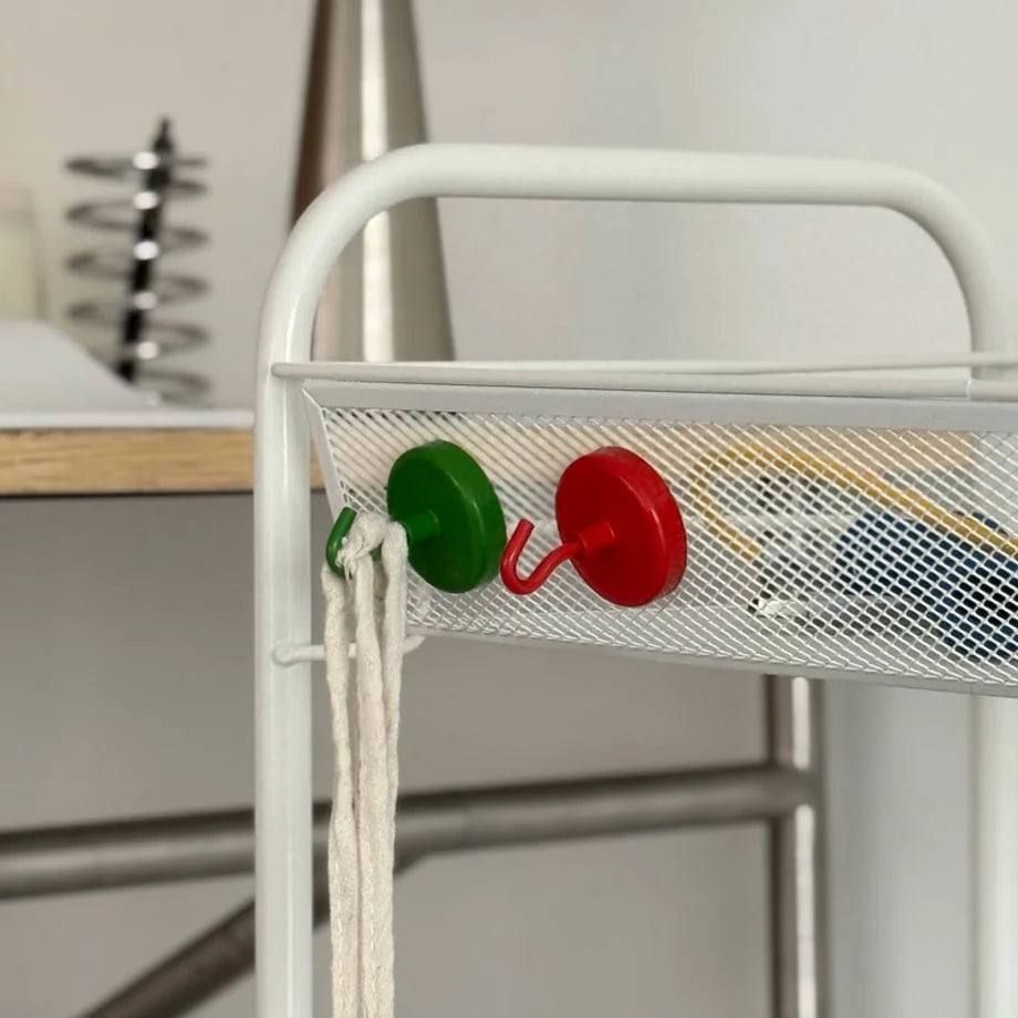 Close-up of red and green magnetic hooks attached to the mesh side of a white utility cart holding a string bag - RoomDen