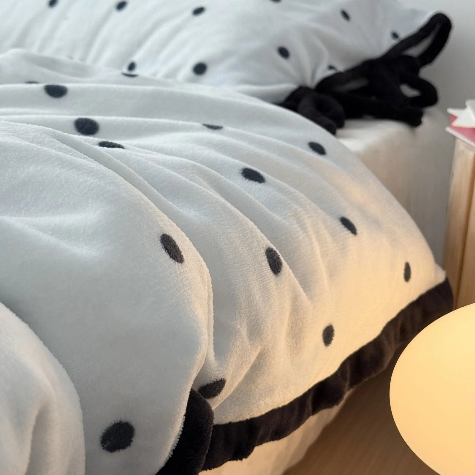 Detail shot of the plush texture and black trim of the Light Blue Polka Dot Flannel Fleece Duvet Cover under warm light.