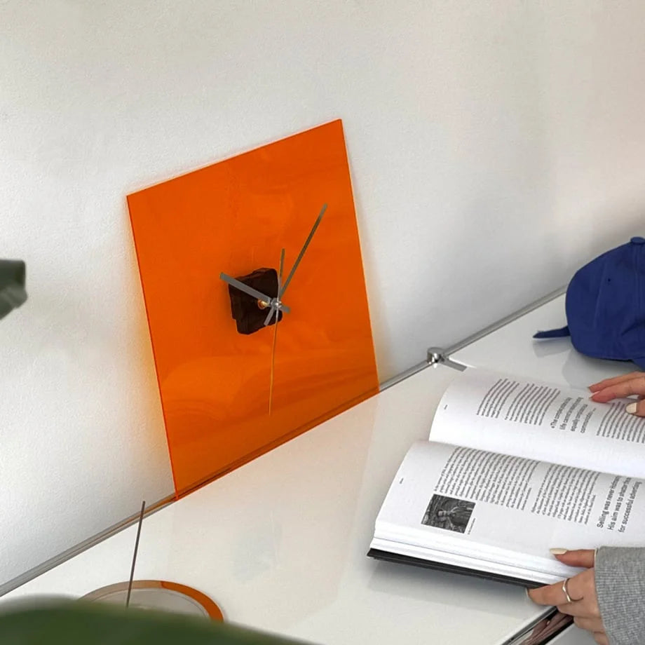 Vivid Orange square clock on a cabinet with a person opening a book next to it. - RoomDen