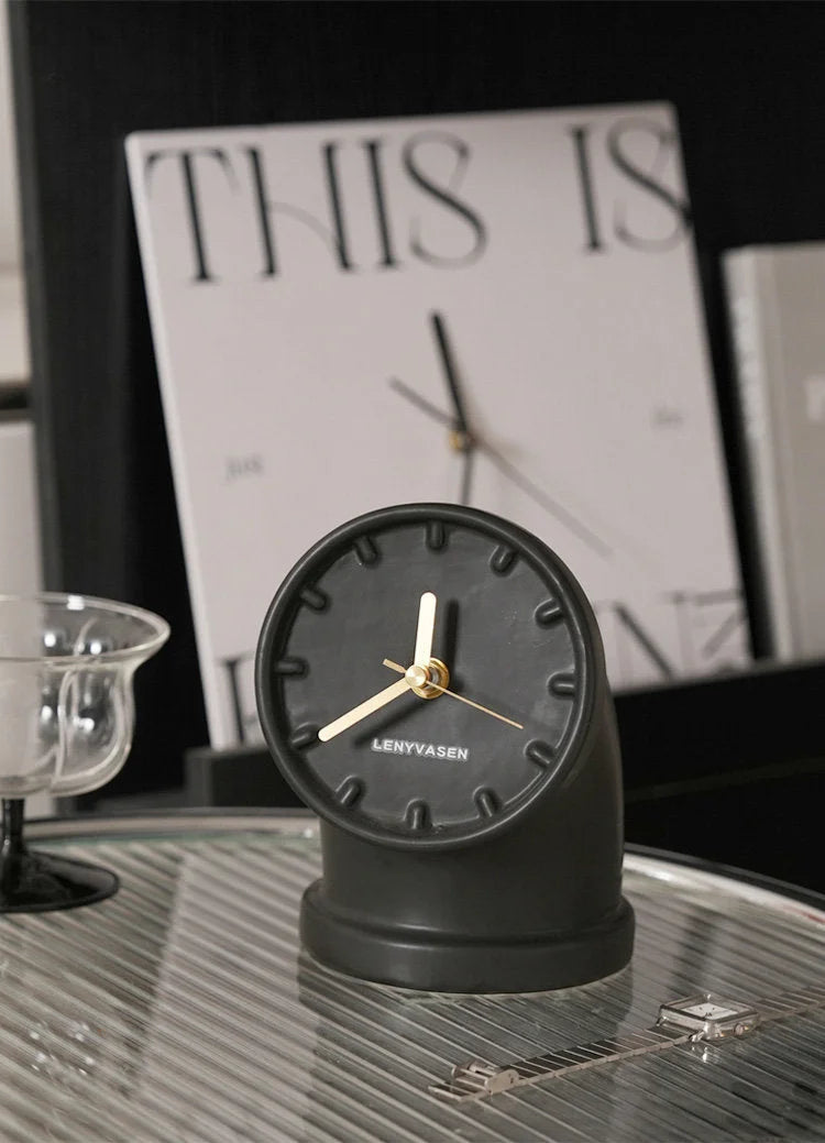 Matte black Industrial Pipe Ceramic Table Clock with gold hands on a glass tray in a modern interior setting - RoomDen