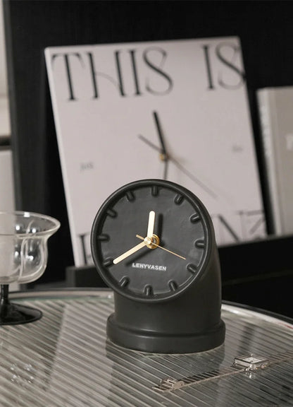 Matte black Industrial Pipe Ceramic Table Clock with gold hands on a glass tray in a modern interior setting - RoomDen