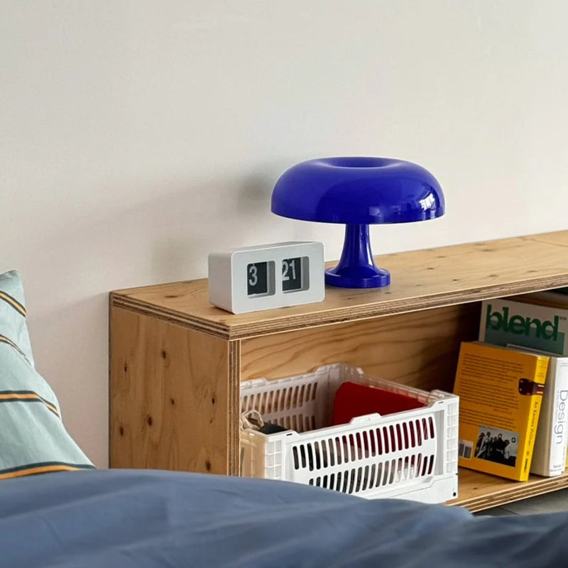 Cobalt blue mushroom lamp glowing on a bedside table next to a flip clock, a warm pool of light in a calm Japandi bedroom — RoomDen.