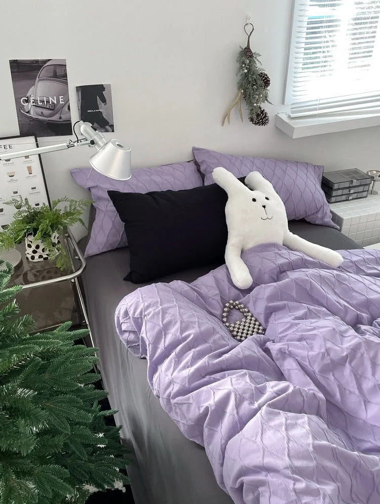 Angled shot of the lavender bedding set in a modern dorm-style room with a desk lamp and wall art. - RoomDen