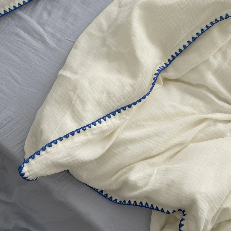 Detail of the cream white duvet cover with blue embroidered edge, showing the soft crinkled texture.