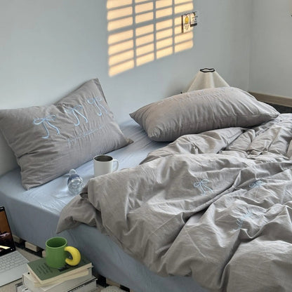 A beige washed cotton bedding set with light blue embroidered bows, styled on a bed for a soft, neutral look. - RoomDen