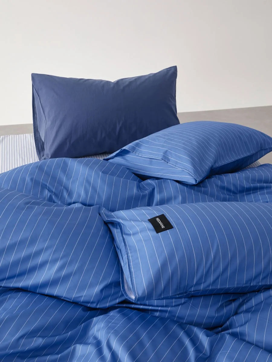 Close-up detail of the layered pillowcases in the Denim Blue Pinstripe Washed Cotton Bedding Set, one striped and one solid - RoomDen.