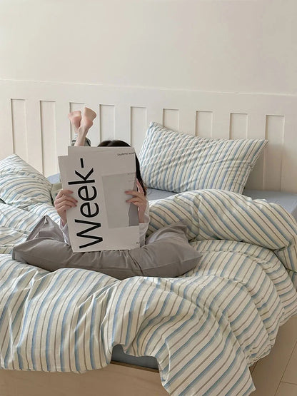 A person reading in bed, surrounded by the cozy Blue Striped Washed Cotton Bedding. - RoomDen