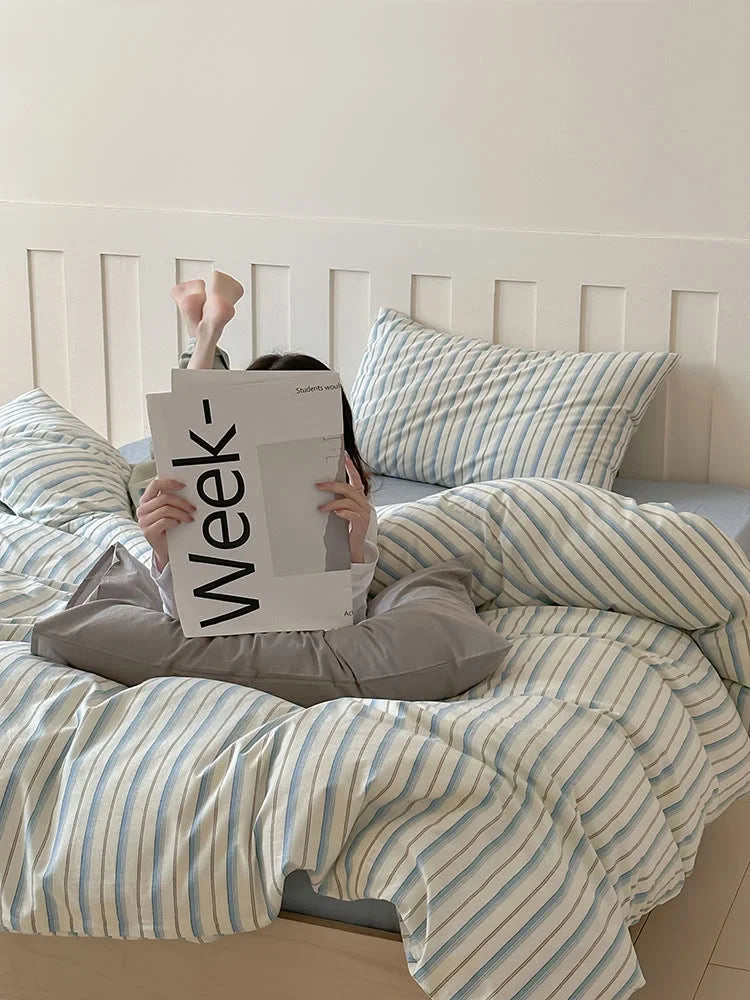A person reading in bed, surrounded by the cozy Blue Striped Washed Cotton Bedding. - RoomDen
